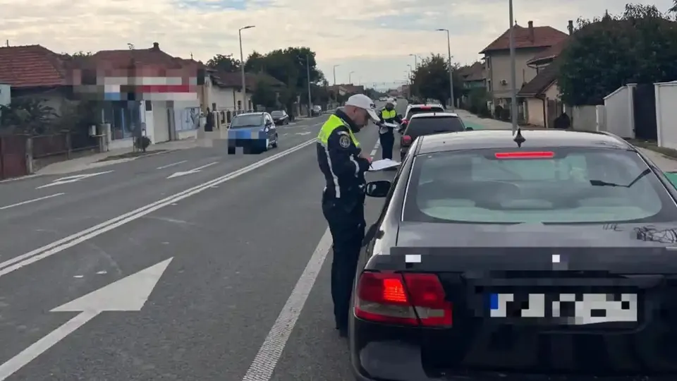 Un autoturism negru se află pe marginea drumului, iar două persoane cu veste reflectorizante stau lângă vehicule.