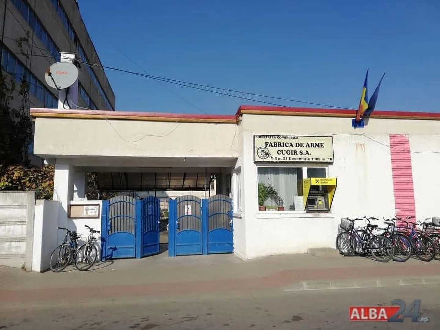 O clădire albă are o poartă albastră, o firmă pe fațadă și mai multe biciclete parcate în față.