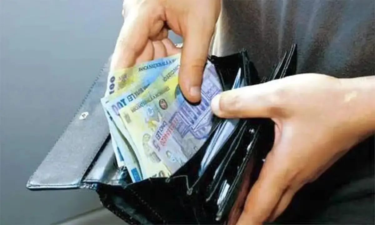 Două mâini țin o bancnotă și un portofel negru deschis, din care se văd și alte bancnote.