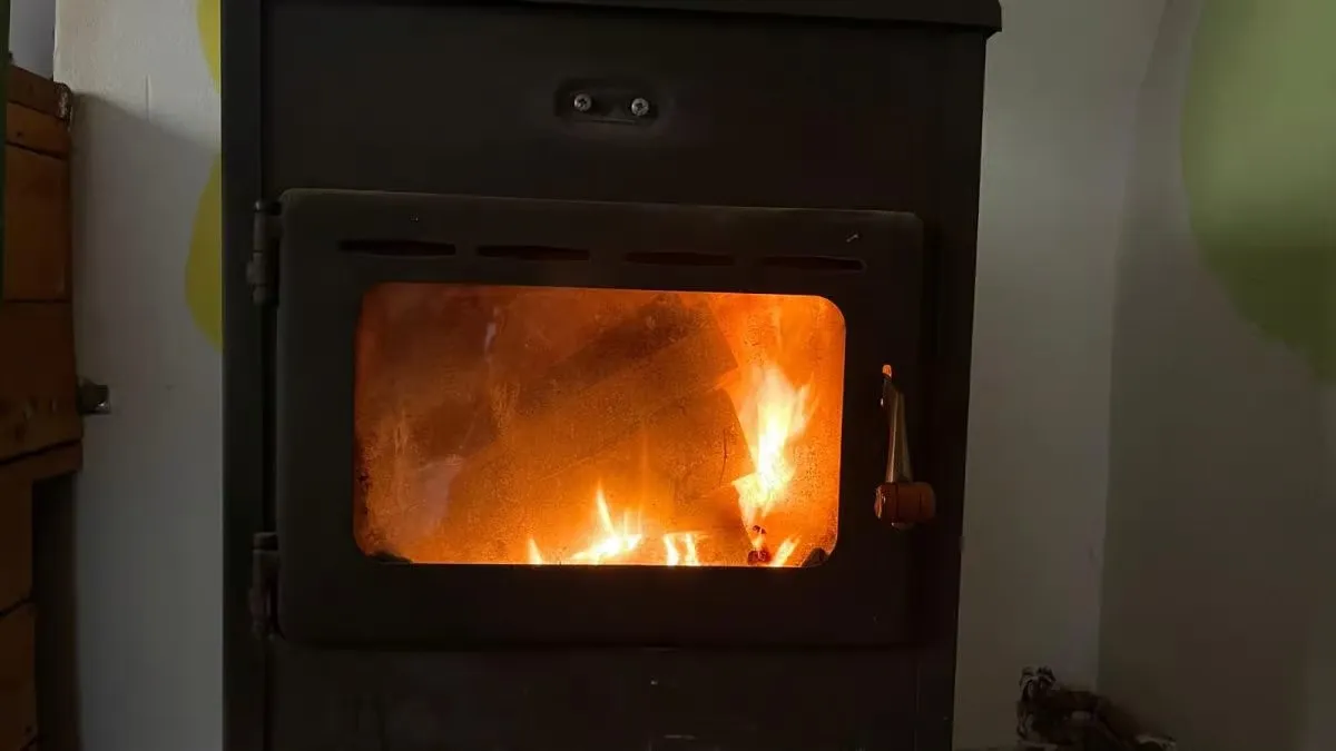 O sobă neagră are o fereastră dreptunghiulară prin care se văd flăcări portocalii; în stânga se află un dulap maro.