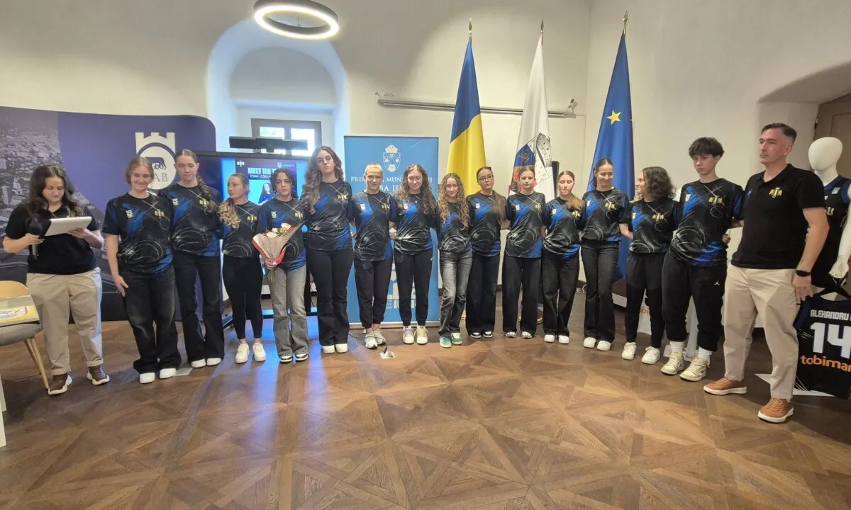 Un grup de persoane stă în rând, majoritatea purtând uniforme sport închise la culoare; câteva țin buchete, iar steaguri sunt așezate în spatele lor.