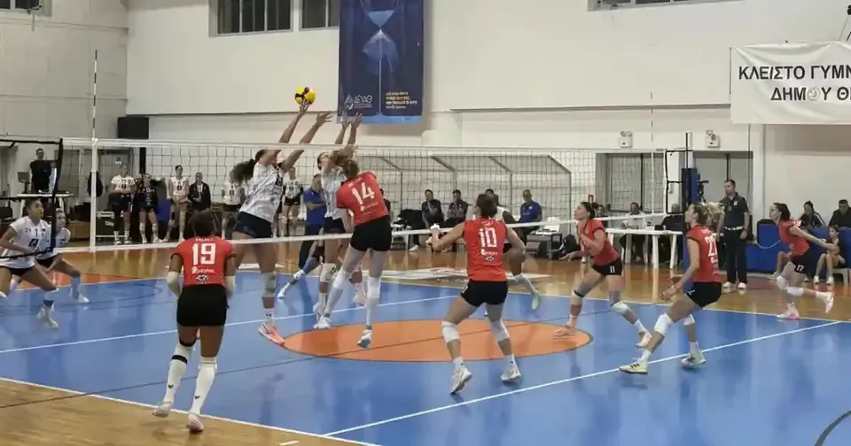 Mai multe jucătoare de volei dispută o fază la fileu, într-o sală cu teren albastru și tribune în fundal.