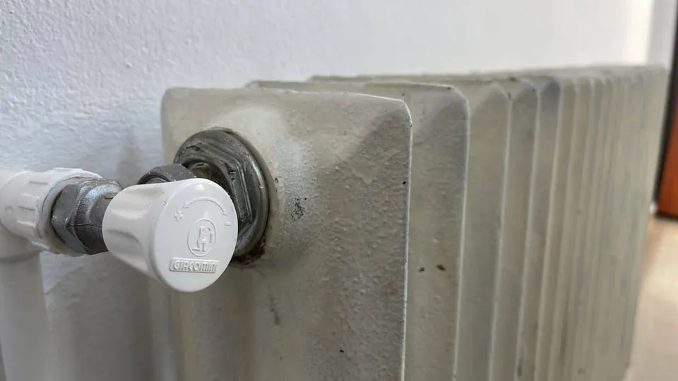 Un calorifer gri, cu aripioare verticale, are în partea stângă un robinet alb montat pe o conductă.