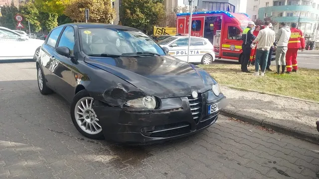 Un autoturism negru cu partea frontală avariată este oprit lângă bordură; în fundal se văd autospeciale și mai multe persoane.