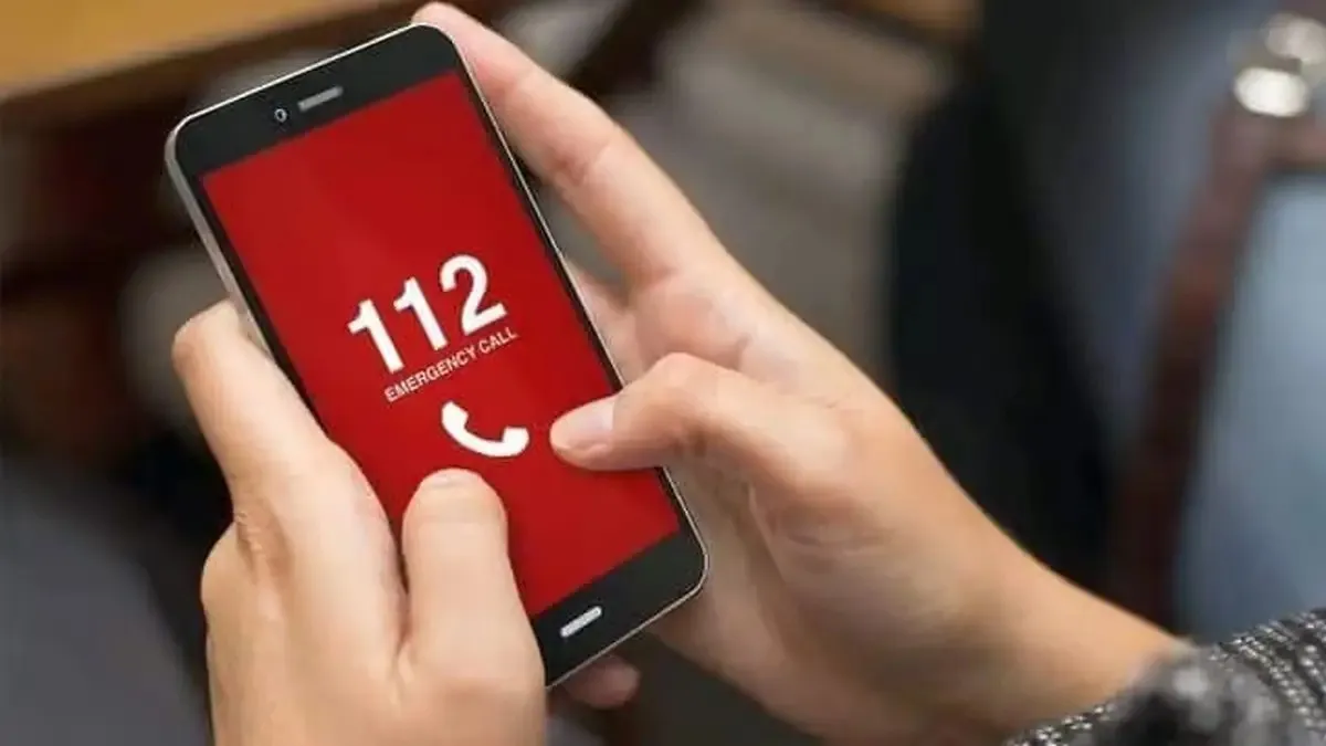 Două mâini țin un telefon cu ecran roșu, pe care apar cifrele 112 și un simbol alb de receptor.