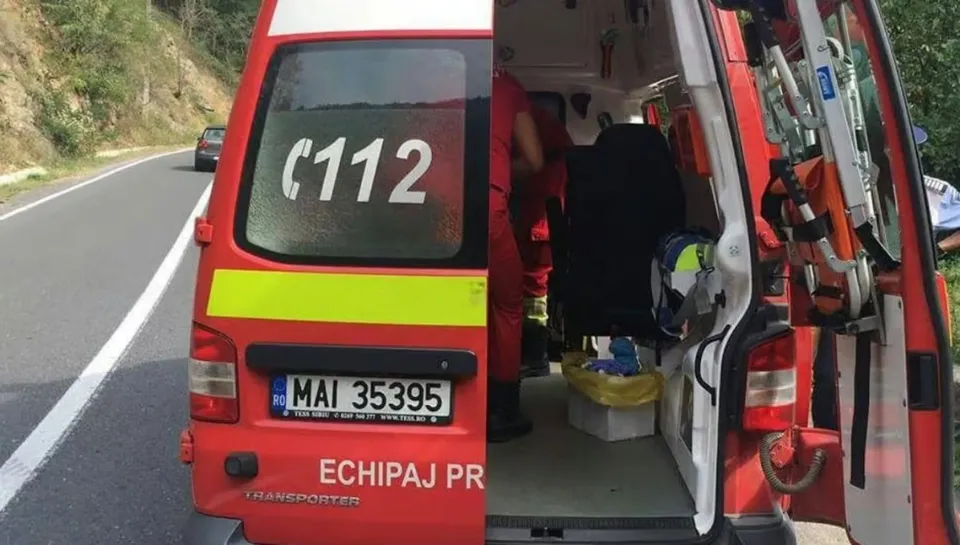 O autospecială roșie cu ușile din spate deschise este oprită pe șosea, iar o persoană îmbrăcată în negru se află în interior.