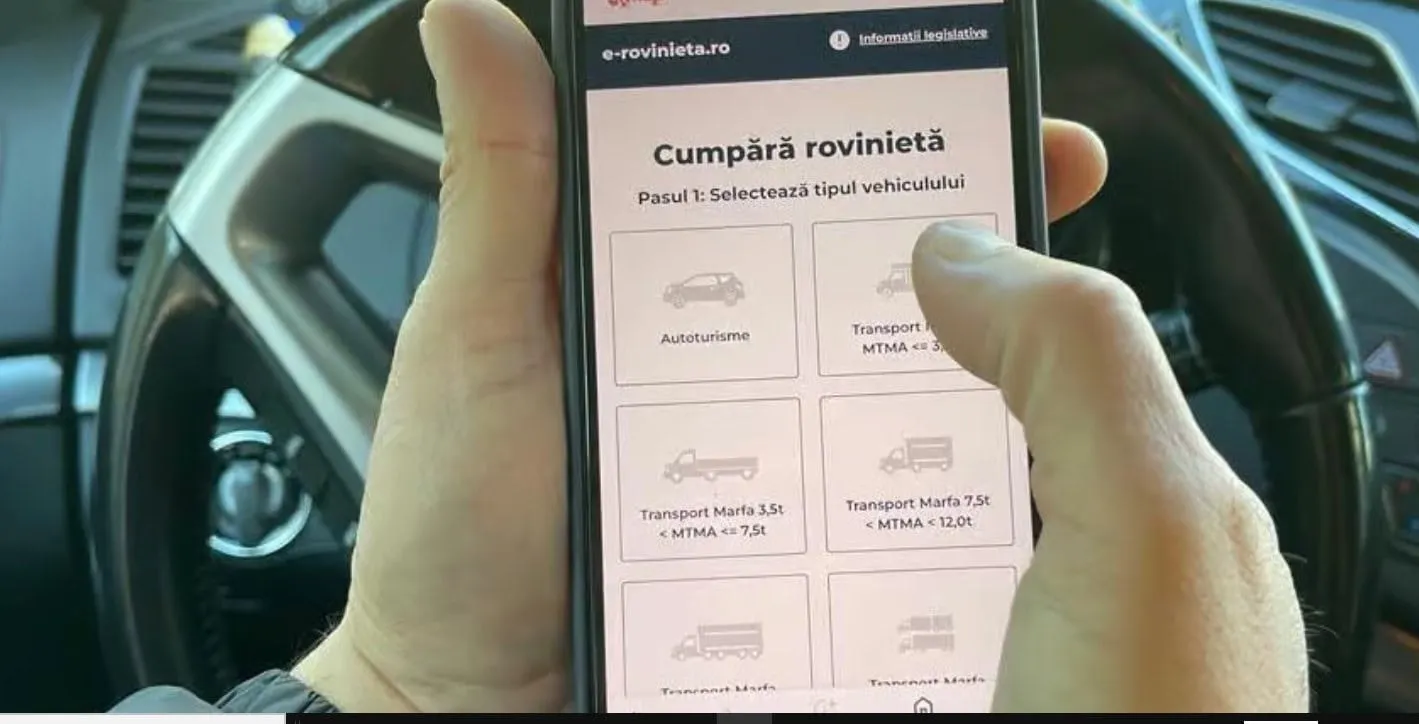 Două mâini țin un telefon cu o pagină de cumpărare a rovinietei pe ecran, în fața unui volan.