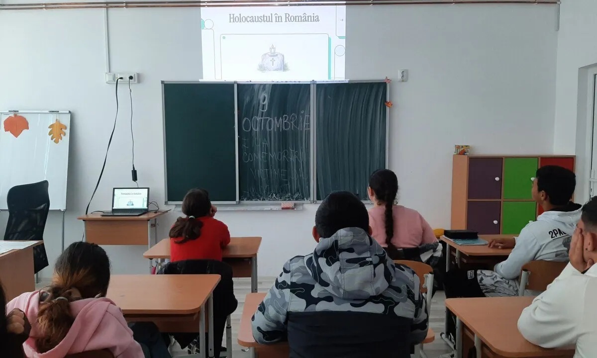 Mai mulți elevi stau la mese orientate spre o tablă, iar o imagine este proiectată pe peretele din față.