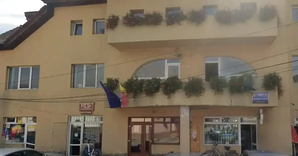 O clădire galbenă cu ferestre, balcoane cu jardiniere, două steaguri și mai multe intrări ocupă imaginea.