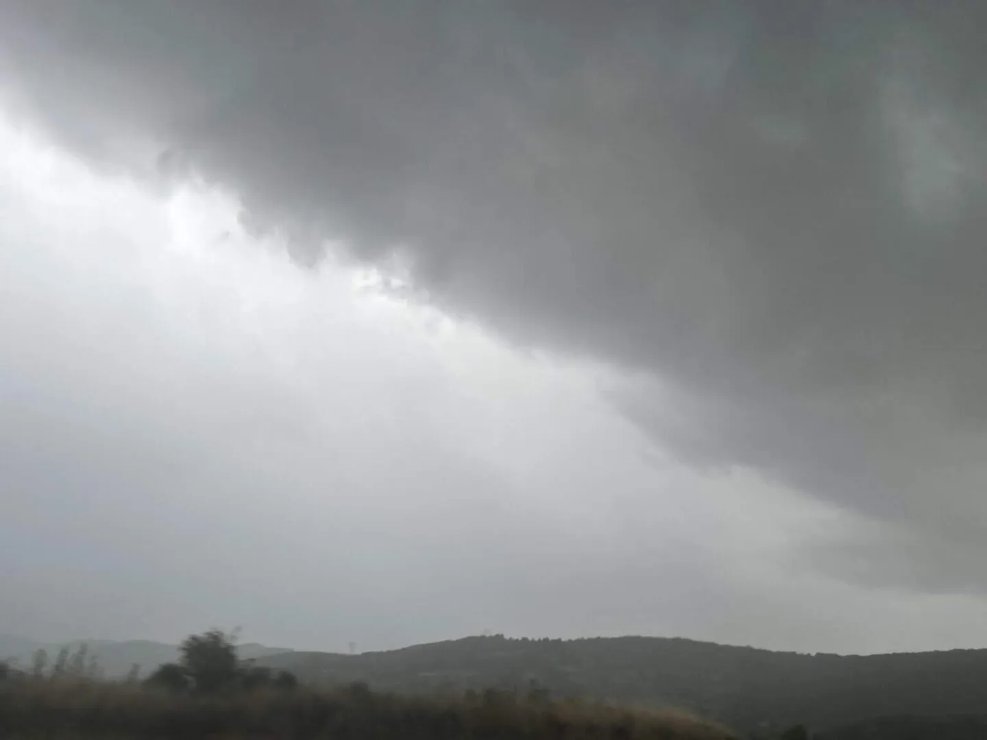 Nori cenușii acoperă cerul deasupra unor dealuri întunecate, iar în prim-plan se văd siluete de arbori și vegetație joasă.