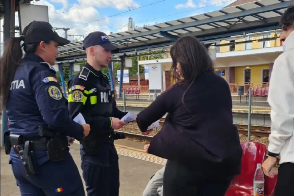 Doi polițiști în uniforme stau lângă o femeie așezată pe un scaun roșu; unul dintre polițiști ține foi, iar femeia întinde mâna spre el.