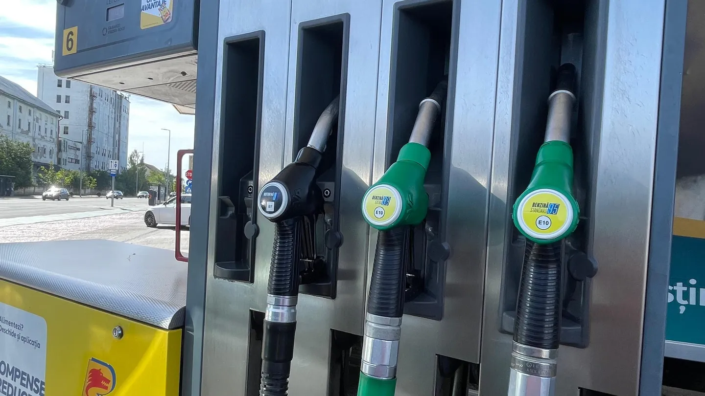 Trei pistoale de alimentare, unul negru și două verzi, sunt așezate în suporturile unui distribuitor de carburanți.