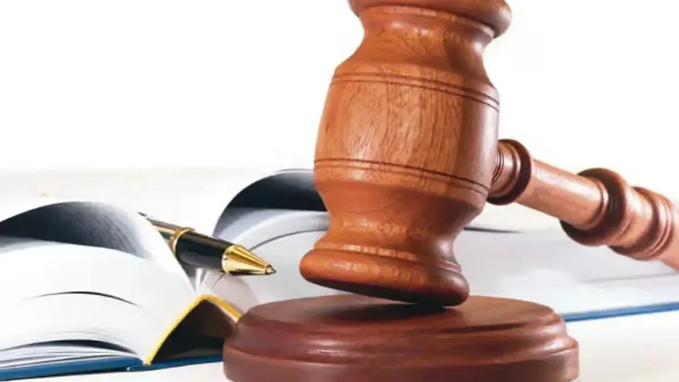 Un ciocănel din lemn se află deasupra unei baze rotunde, lângă o carte deschisă și un stilou.