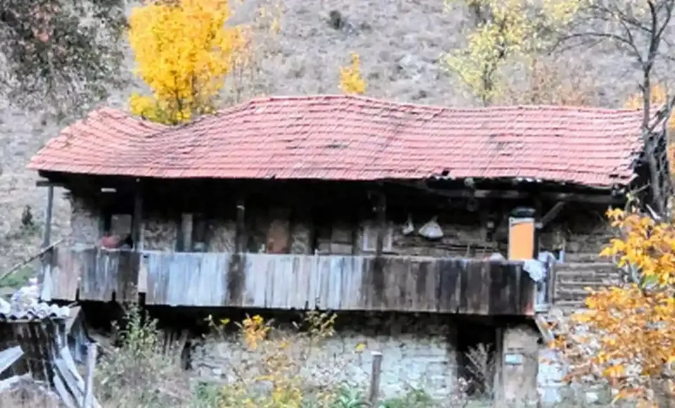 O casă cu acoperiș roșu și balcon din lemn se află între copaci cu frunze galbene.