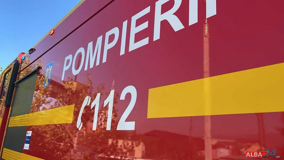 O autospecială roșie cu dungă galbenă și inscripțiile „POMPIERI” și „112” ocupă cadrul, sub un cer albastru.