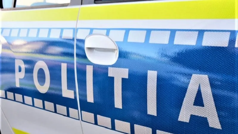 Prim-plan al portierei unui vehicul alb, cu dungi albastre și galbene și inscripția „POLIȚIA” pe lateral.