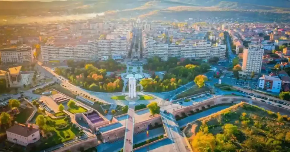 Vedere aeriană cu blocuri, clădiri, drumuri, spații verzi și un monument alb amplasat într-un sens giratoriu.