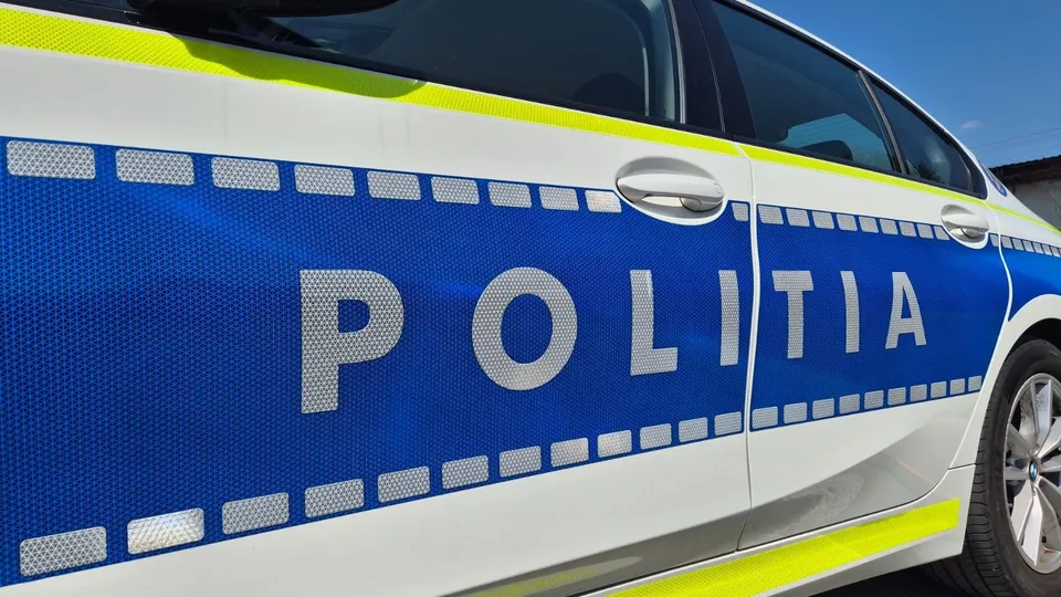 Prim-plan lateral al unui autoturism alb, cu panou albastru inscripționat „POLIȚIA”, dungi galbene reflectorizante, geamuri închise la culoare și o roată.