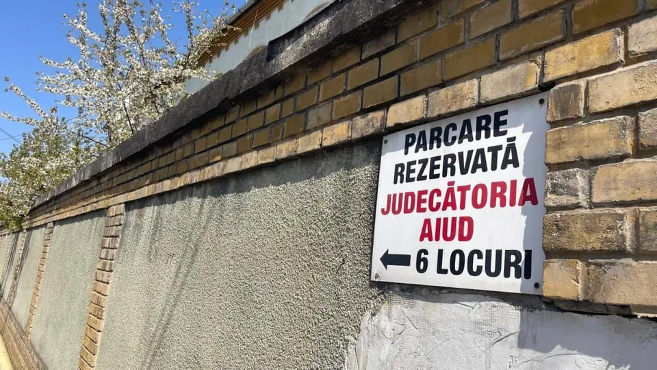 Un indicator dreptunghiular alb, cu text negru și roșu, este montat pe un zid de cărămidă și tencuială.