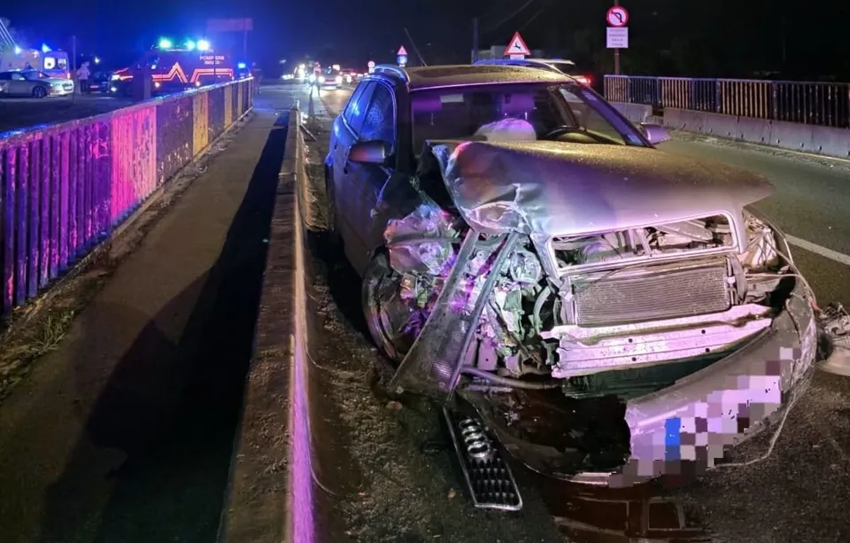 Un autoturism cu partea din față grav avariată se află lângă un parapet, iar în fundal se văd vehicule cu lumini aprinse.
