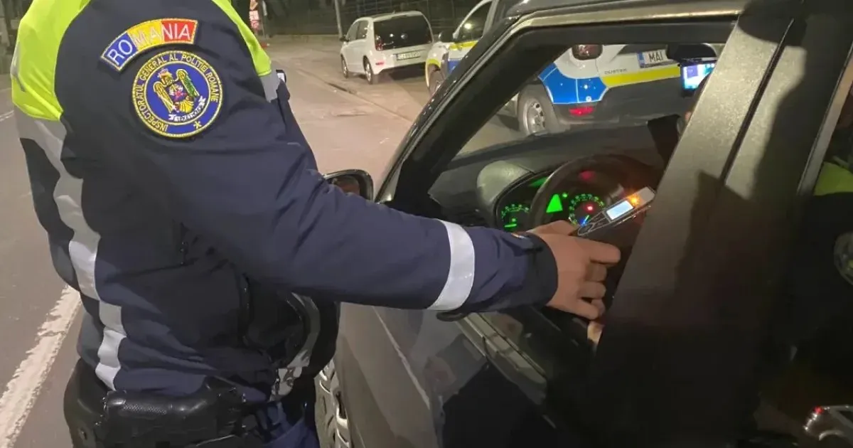 O persoană în uniformă albastră cu elemente reflectorizante ține mâna la fereastra unui autoturism negru, lângă un dispozitiv mic.