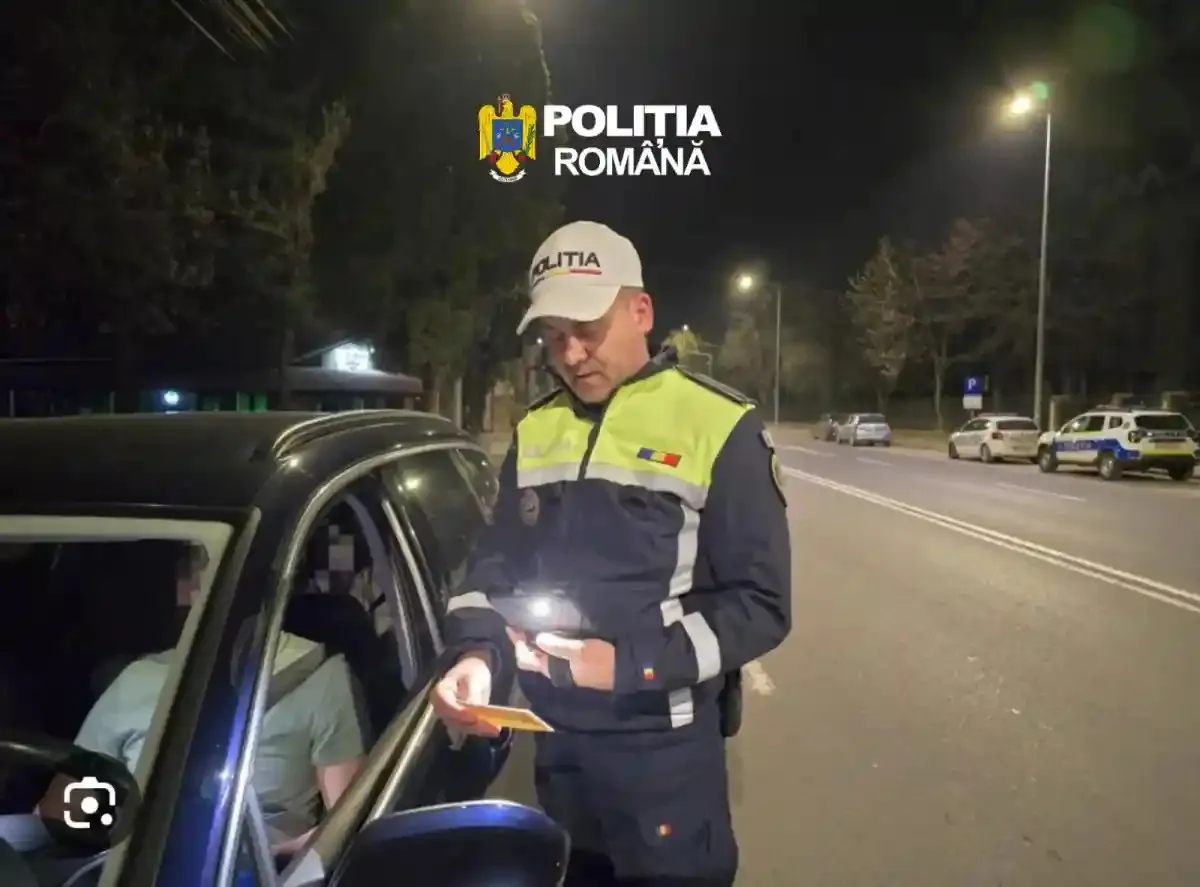 Un polițist în uniformă reflectorizantă stă lângă o mașină, iar o persoană se află la volan; pe șosea se văd alte vehicule și lămpi.
