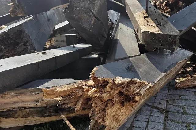 Grinzi de lemn rupte și așchiate sunt îngrămădite peste un pavaj din piatră; în prim-plan se vede capătul sfărâmat al unei grinzi.