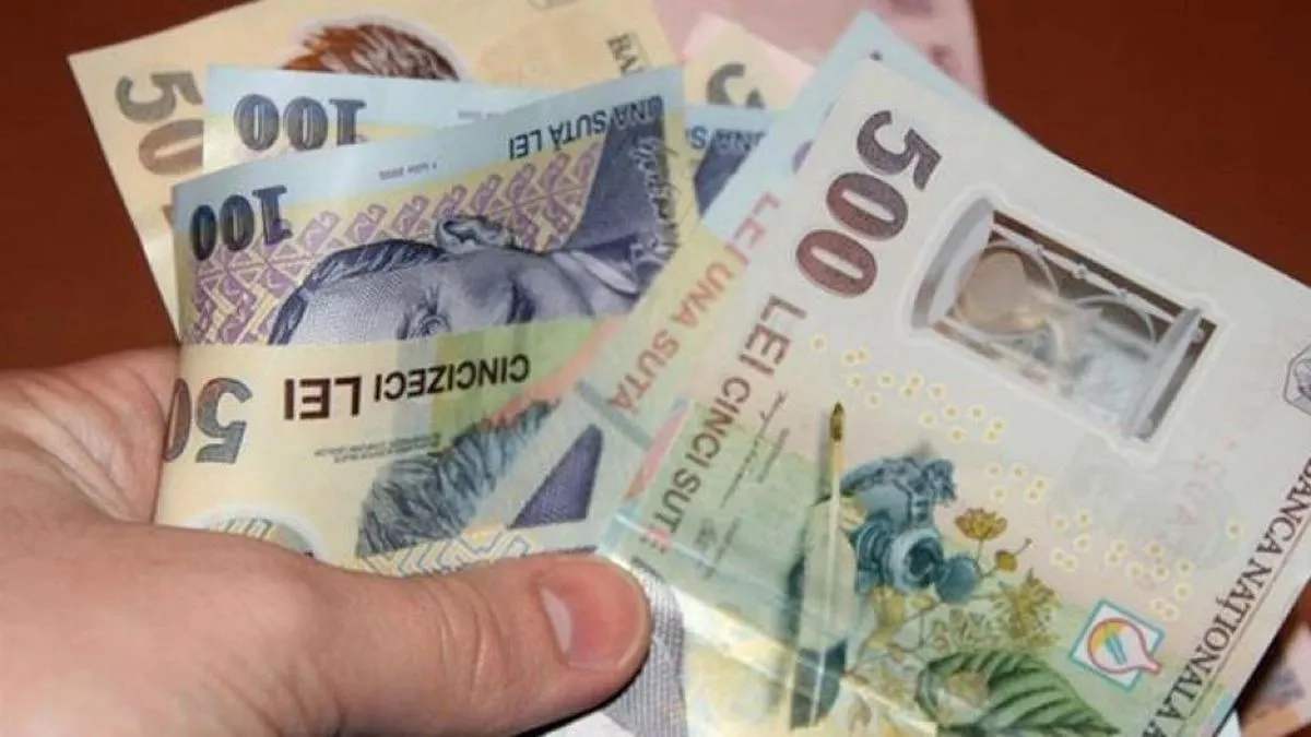 O mână ține mai multe bancnote românești de valori diferite, suprapuse și desfăcute în evantai.