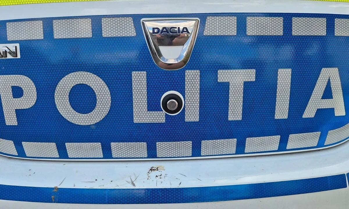 Prim-plan al părții frontale a unei mașini albastre și albe, cu sigla Dacia, inscripția „POLIȚIA”, marcaje reflectorizante și bară zgâriată.