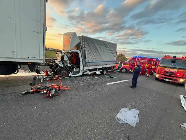 O autoutilitară cu partea din față avariată se află lângă o remorcă; pe șosea sunt resturi, iar în dreapta se văd autospeciale și persoane.