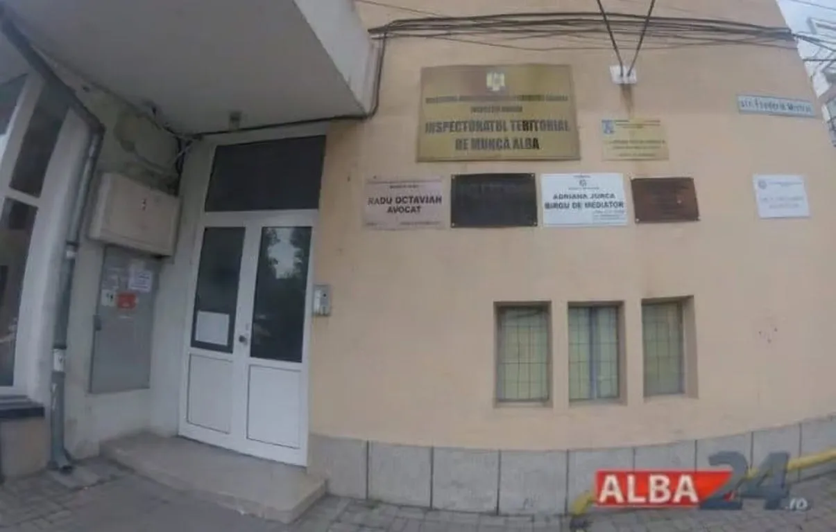 Fațada unei clădiri are o ușă albă cu geamuri, trei ferestre înguste și mai multe plăcuțe montate pe perete.