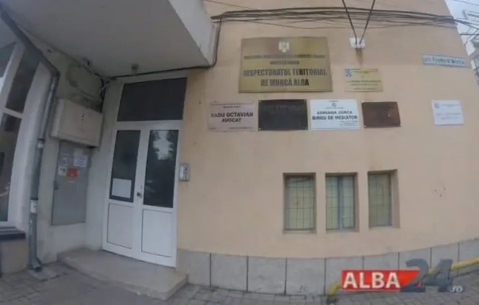 Fațada unei clădiri are o ușă albă cu geamuri, trei ferestre înguste și mai multe plăcuțe montate pe perete.
