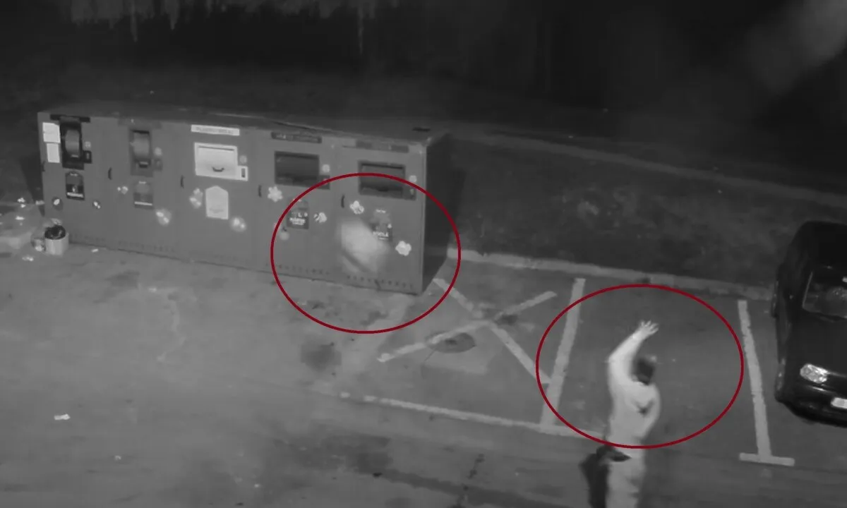 Imagine alb-negru cu mai multe containere metalice, o persoană cu un braț ridicat, un autoturism parțial vizibil și marcaje pe asfalt.