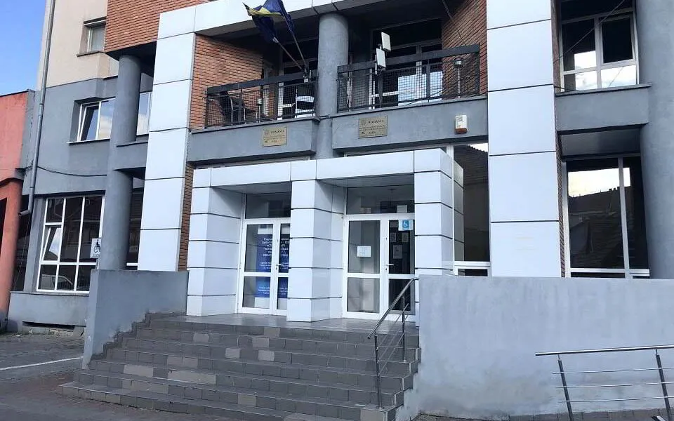 Fațada unei clădiri cu trepte, uși vitrate, ferestre, coloane, balcoane metalice și o rampă cu balustradă.