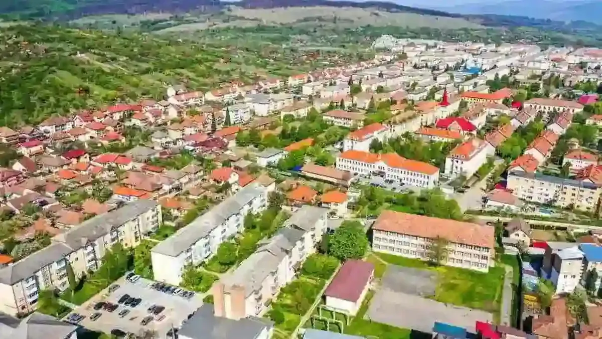 Imagine aeriană cu blocuri, case cu acoperișuri roșii, străzi, mașini parcate și zone verzi.