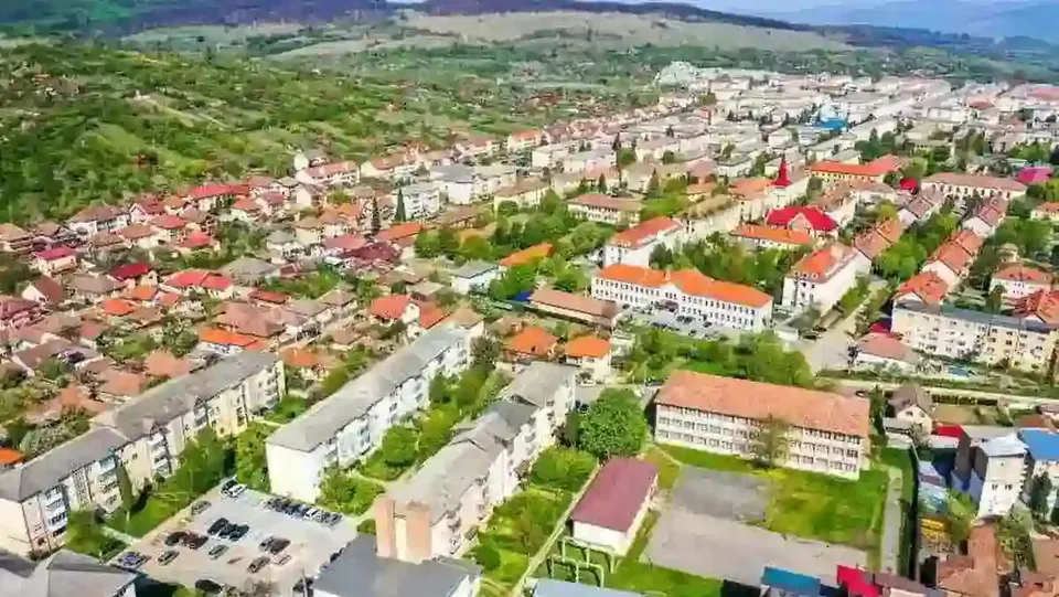 Imagine aeriană cu blocuri, case cu acoperișuri roșii, străzi, mașini parcate și zone verzi.