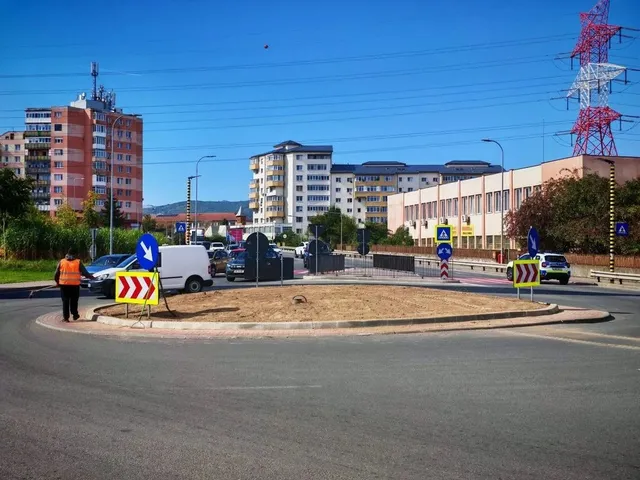 Un sens giratoriu are o insulă centrală cu pământ expus, semne temporare de circulație și un lucrător îmbrăcat cu vestă portocalie.