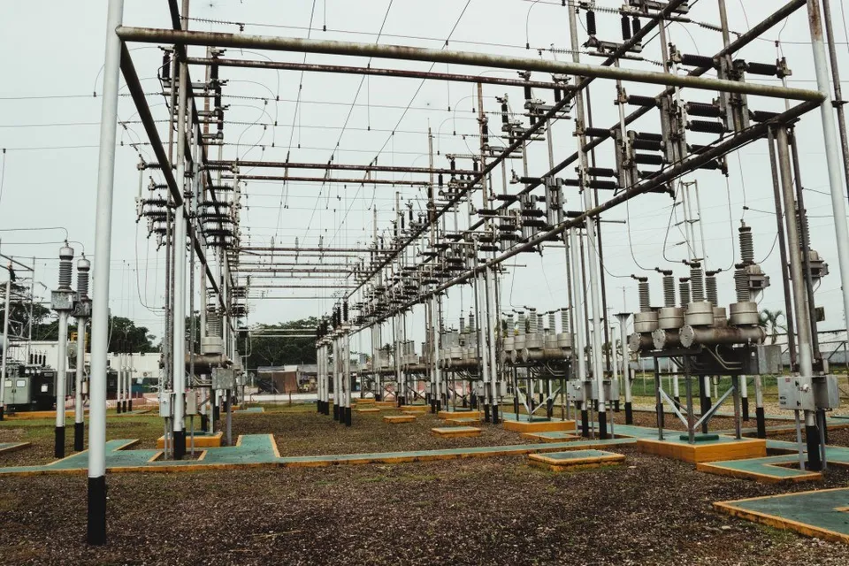 O stație electrică are structuri metalice, cabluri aeriene, izolatoare, transformatoare și platforme delimitate, amplasate pe un teren acoperit cu pietriș.