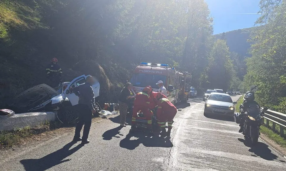 Un autoturism avariat se află lângă carosabil, iar mai mulți salvatori manevrează o targă în fața unei ambulanțe, printre vehicule oprite.