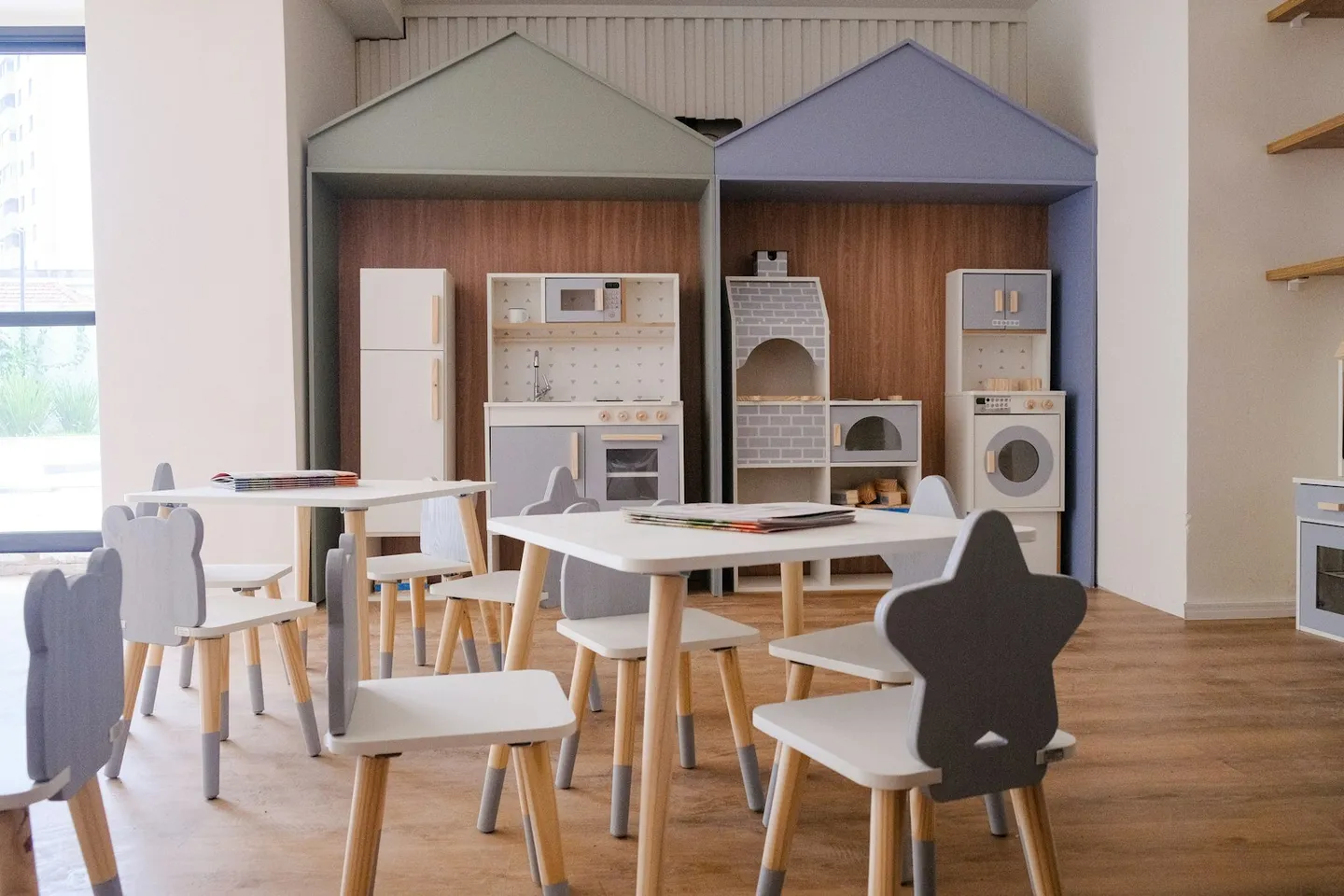 O sală cu mese și scaune mici, mobilier de bucătărie de jucărie și structuri decorative în formă de case.