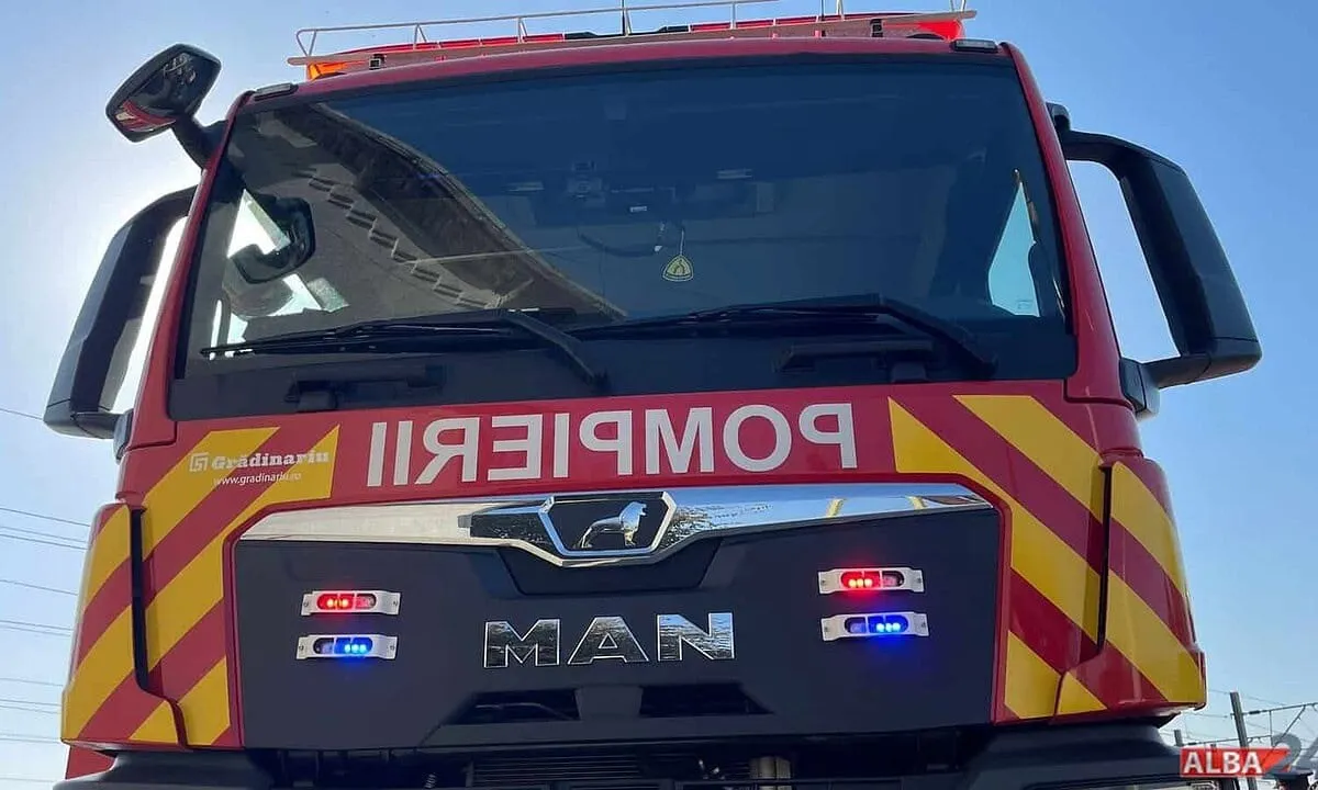 Un camion roșu cu benzi galbene este fotografiat din față, cu parbriz mare, lumini și inscripția MAN, pe un fundal cu cer albastru.