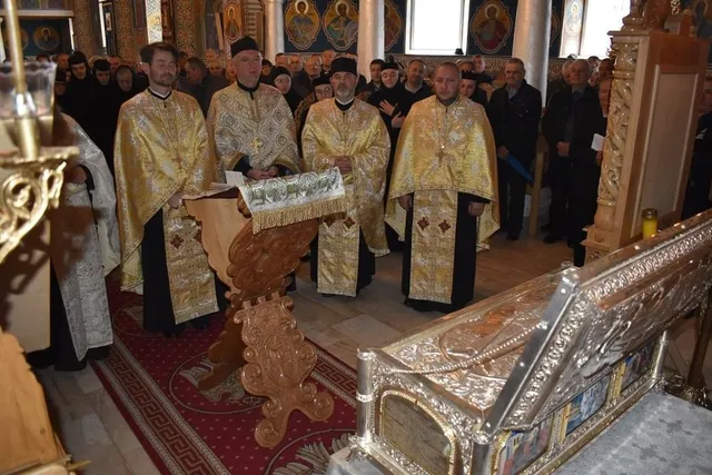 Patru bărbați în veșminte aurii stau lângă un pupitru sculptat, iar în prim-plan se află un obiect metalic ornamentat.