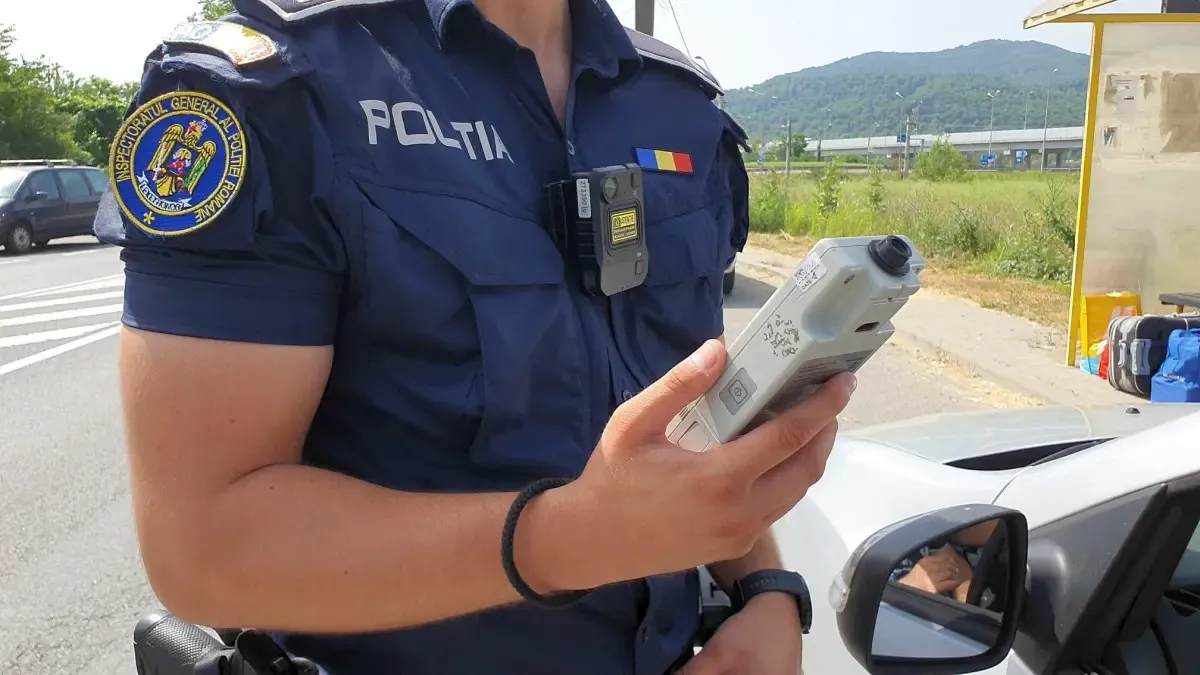 Un polițist în uniformă ține un aparat electronic lângă o mașină, pe marginea unui drum.
