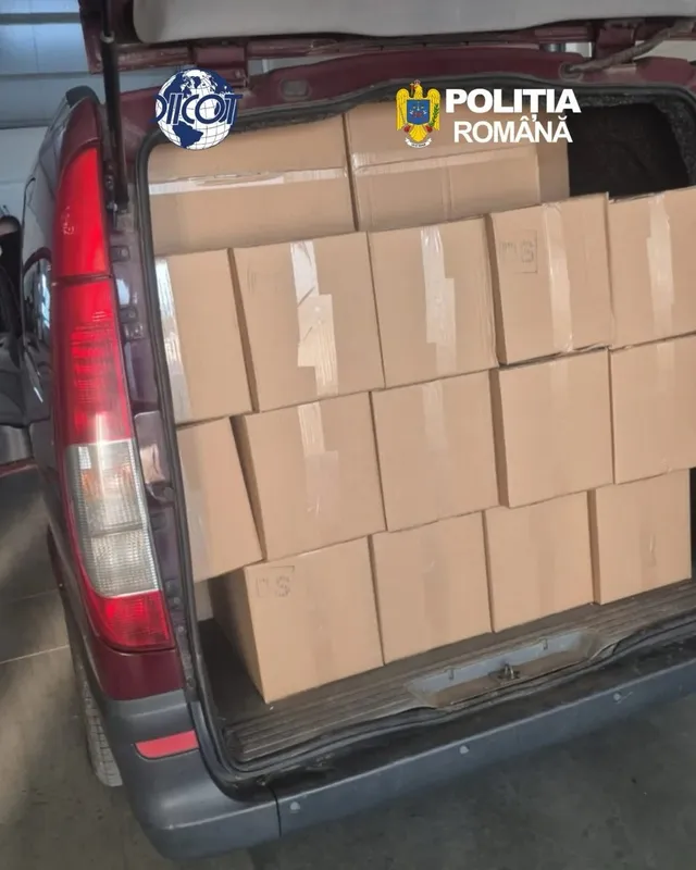 În compartimentul din spate al unei autoutilitare cu ușa ridicată sunt stivuite cutii de carton; pe imagine apar două sigle.