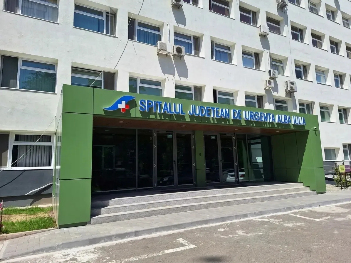 O clădire cu multe ferestre are o intrare verde, trepte largi și o zonă pavată în față.