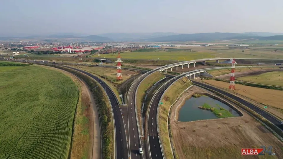 O imagine aeriană arată șosele curbe și pasaje, câmpuri verzi și maronii, un bazin cu apă și stâlpi metalici.