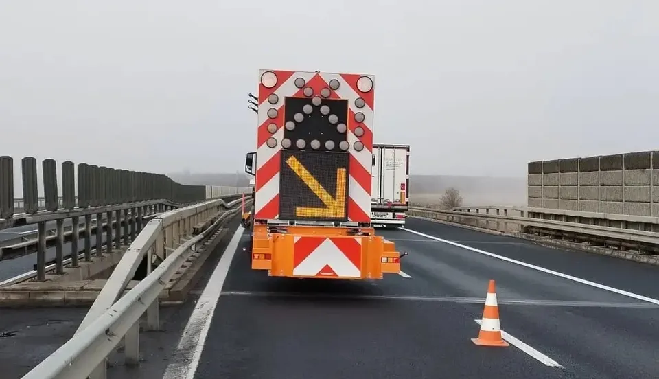 Un vehicul cu panou de semnalizare ocupă o bandă de autostradă, iar un con portocaliu se află în spatele lui, lângă marcaj.