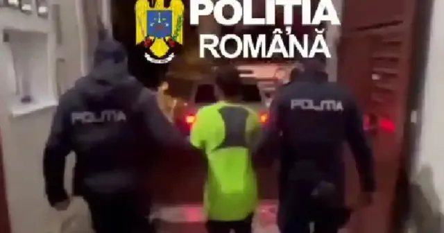 Două persoane în jachete negre cu inscripția „POLIȚIA” merg de o parte și de alta a unei persoane în haină verde fluorescentă.