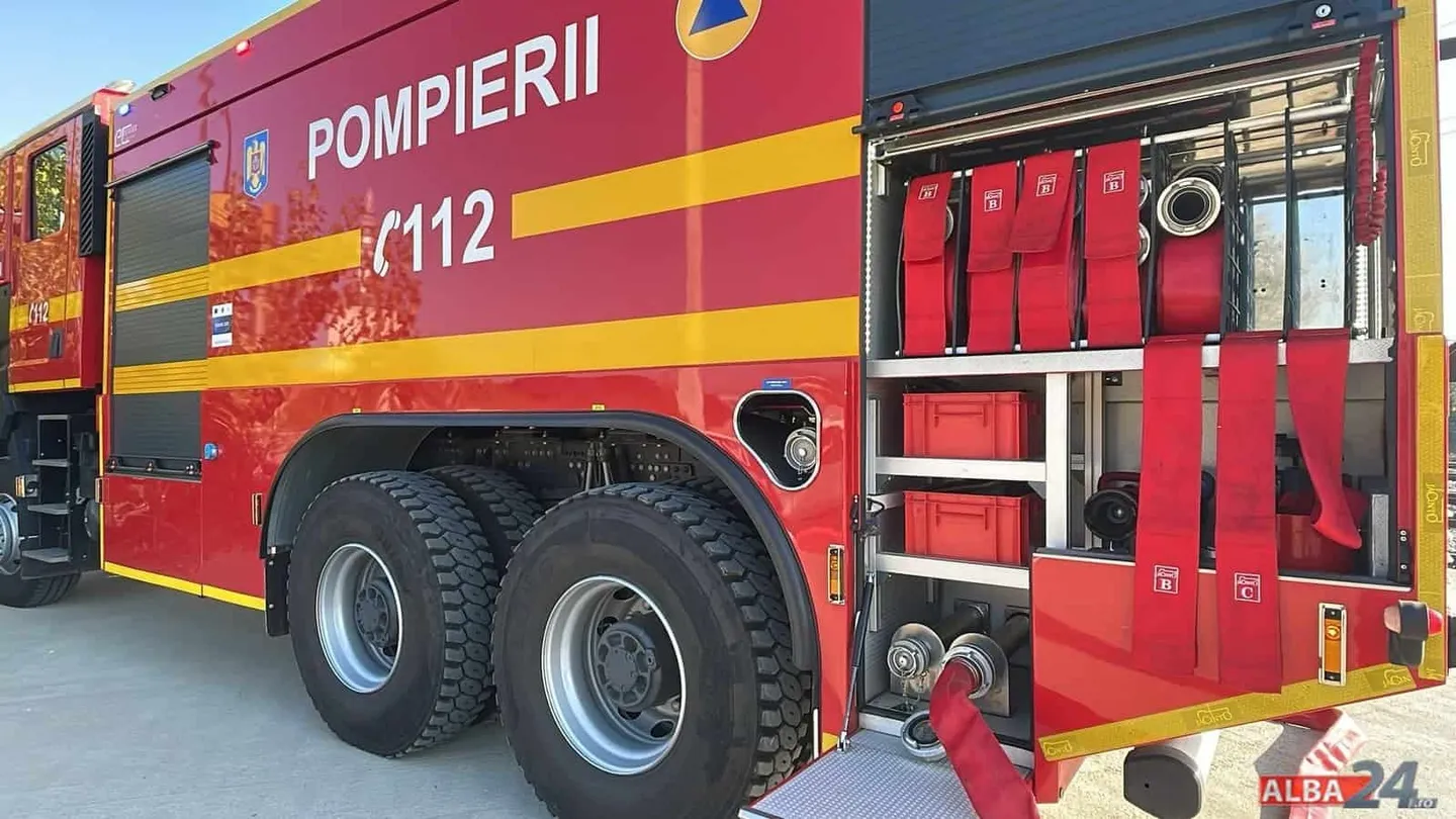 O autospecială roșie cu inscripția „POMPIERII 112”, compartimente laterale deschise, furtunuri, recipiente și două roți mari este parcată pe asfalt.