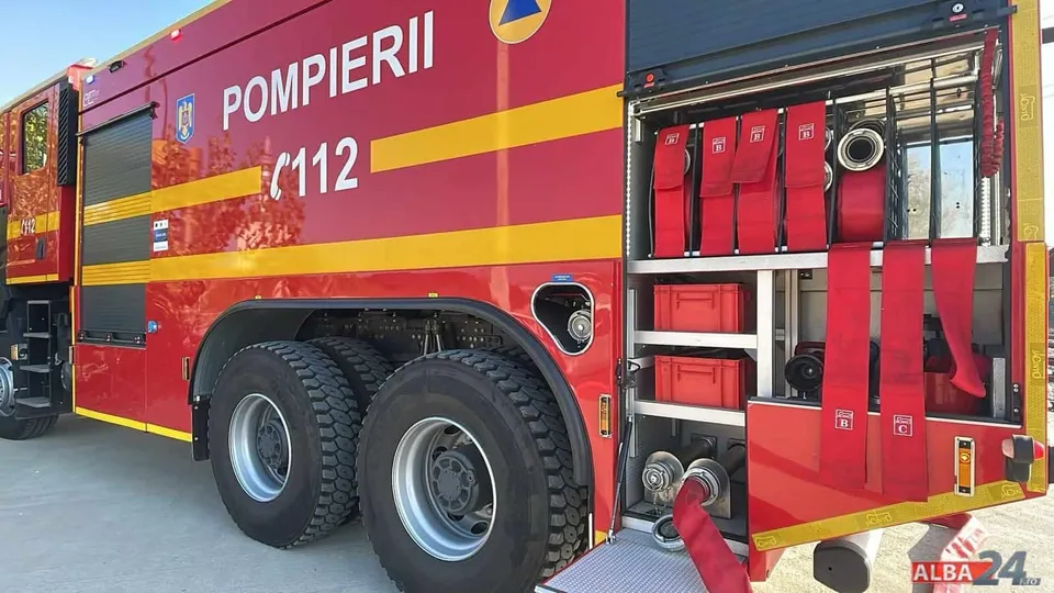 O autospecială roșie cu inscripția „POMPIERII 112”, compartimente laterale deschise, furtunuri, recipiente și două roți mari este parcată pe asfalt.